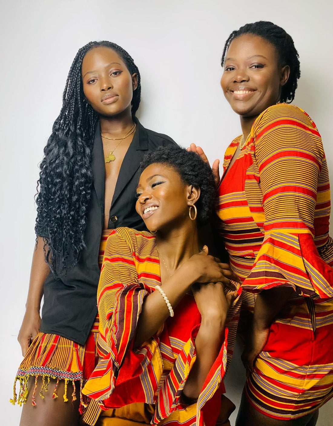 3 ladies wearing stripped red, brown and yellow kikoy print material. wrap top, high waisted shorts, high waisted frill skirt. womenwear. summer inspiration. picnicfashion outfir. african print loving
